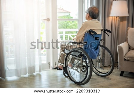 Asian senior man disabled sitting alone sitting in wheelchair looking through window at hospital, lonely elder thoughtful sad old man look outside windows in bedroom at retirement home, feel depressed