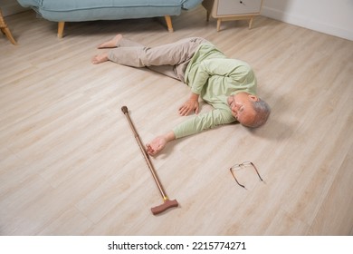 Asian Senior Man Falling Down Lying On Floor At Home Alone With Wooden Walking Stick In Living Room, Elderly Man Headache After Fall Down, Health Care And Medicine Concept