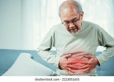 Asian Senior man feel stomachache. Older mature male touch belly while sitting on sofa in living room at home. Bowel problem health care and medical insurance concept. - Powered by Shutterstock