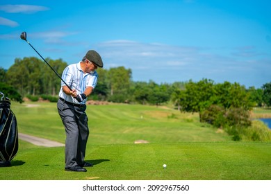 Asian Senior Man Holding Golf Club Hitting Golf Ball On Fairway At Country Club In Sunny Day. Healthy Elderly Male Golfer Enjoy Outdoor Activity Sport Golfing At Golf Course On Summer Vacation