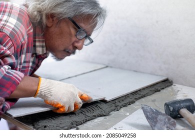 Asian Senior Man Laying Ceramic Tiles On The Floor, Home Repair By Yourself, Selective Focus