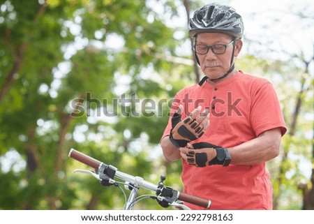 Asian Senior Man putting bicycle gloves before riding on bicycle in park outdoor.