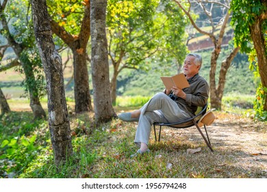 Asian senior man sitting alone on outdoor chair in nature park with writing or drawing on paper notebook. Healthy elderly retired male relax and enjoy outdoor leisure activity hobby in sunny day - Powered by Shutterstock