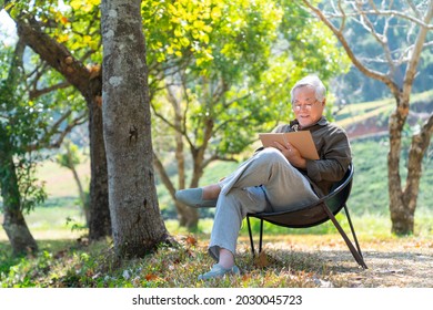 Asian senior man sitting alone on outdoor chair in nature park with writing or drawing on paper notebook. Healthy elderly retired male relax and enjoy outdoor leisure activity hobby in sunny day - Powered by Shutterstock