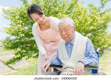 Asian Senior Man Sitting On A Wheelchair With Caregiver