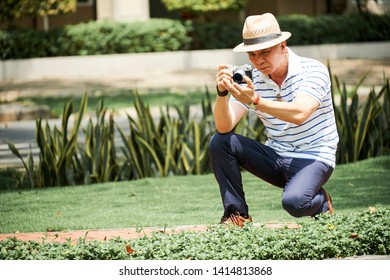 Asian senior man sitting and photographing beautiful nature in summer on his photo camera outdoors - Powered by Shutterstock