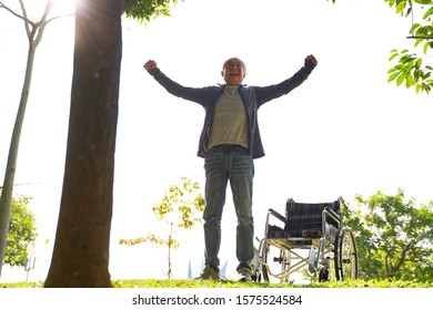 Asian Senior Man Standing By Wheel Chair With Open Arms