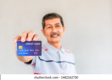 Asian Senior Man Standing Smiling And Hand Holding Credit Card Show With Happiness On Gray Background. Elderly And Credit Card Concept.