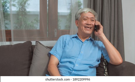 Asian Senior Man Talk On Phone At Home. Asian Senior Older Chinese Male Using Mobile Phone Talking With Family Grandchild Kids While Lying On Sofa In Living Room At Home Concept.