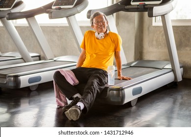 Asian Senior Man Tired Taking Break After Exercise Sitting Or Resting On Treadmill In Fitness Gym . Walking  Workout  . Sport , Trainnig , Retired , Older , Mature, Elderly