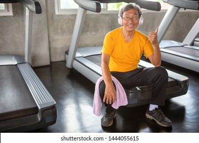 Asian Senior Man Tired Taking Break After Exercise Sitting Or Resting On Treadmill And Show Thumbs Up  In Fitness Gym . Walking  Workout  . Sport , Trainnig , Retired , Older , Mature, Elderly