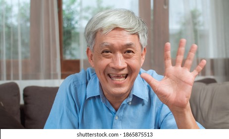 Asian Senior Man Video Call At Home. Asian Senior Older Chinese Male Using Mobile Phone Video Call Talking With Family Grandchild Kids While Lying On Sofa In Living Room At Home Concept.