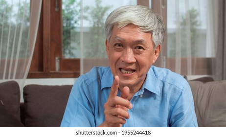 Asian Senior Man Video Call At Home. Asian Senior Older Chinese Male Using Mobile Phone Video Call Talking With Family Grandchild Kids While Lying On Sofa In Living Room At Home Concept.