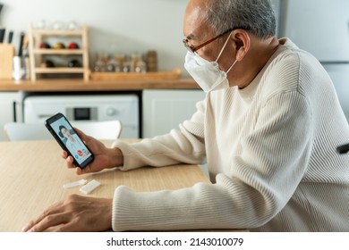 Asian Senior Man Video Call With Doctor In Living Room At Home. Elderly Older Man Patient Consult With Specialist Practitioner After Using ATK Rapid Test Kit To Check Positive 2 Stripe Result At Home.