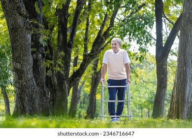 Asian senior man with walker walking alone at the park enjoying beautiful nature and wildlife during summer for light exercise and physical therapy after knee surgery recovery program