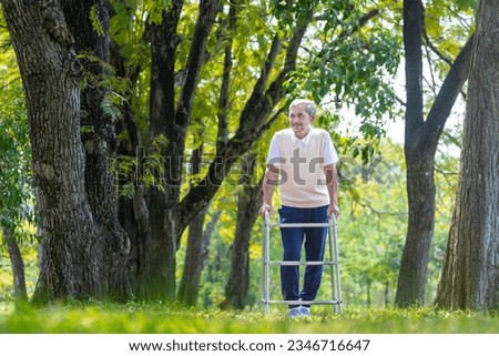 Asian senior man with walker walking alone at the park enjoying beautiful nature and wildlife during summer for light exercise and physical therapy after knee surgery recovery program