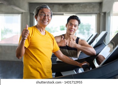 Asian Senior Man Walking Exercise On Treadmill With Personal Trainer Workout In Fitness Gym And Show Thumbs Up . Sport Trainnig , Retired , Older , Mature, Elderly , Smiling .rehab