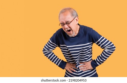 Asian Senior Man Wearing Glasses Standing Face Expression With A Stomachache Isolated On Yellow Background. Elderly Male Feeling Pain In His Stomach Ache And Nausea Diarrhea With Sickness From Cancer.