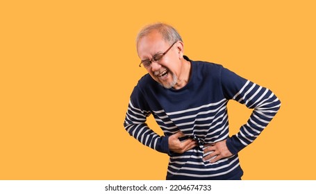 Asian Senior Man Wearing Glasses Standing Face Expression With A Stomachache Isolated On Yellow Background. Elderly Male Feeling Pain In His Stomach Ache And Nausea Diarrhea With Sickness From Cancer.