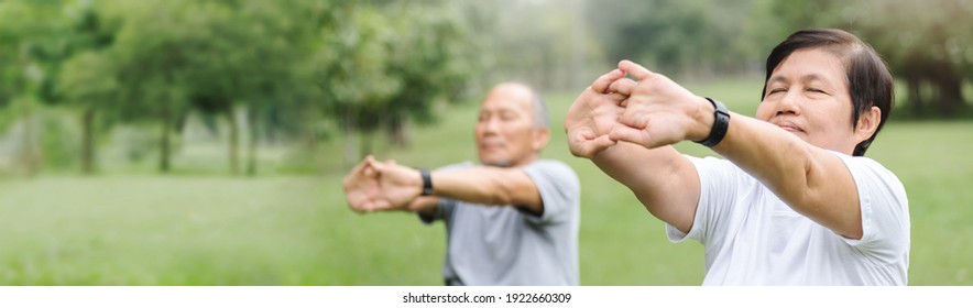 Asian Senior Man And Woman Stretching Hands And Arms Before Exercise At Park. Happy Elderly Couple Enjoying Workout At Outdoor In The Morning. Mature Adult Relaxing And Breathing In Fresh Air. Banner