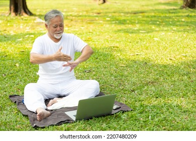 Asian Senior Man Workout And Doing Yoga With Online Training From Laptop Computer In The Park