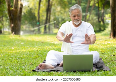 Asian Senior Man Workout And Doing Yoga With Online Training From Laptop Computer In The Park