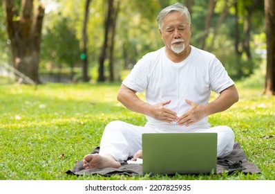 Asian Senior Man Workout And Doing Yoga With Online Training From Laptop Computer In The Park