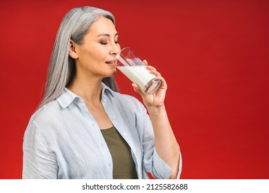 Asian Senior Mature Aged Woman Drinking Milk For Calcium Food And Healthy Lifestyle Concept Isolated On Red Background.