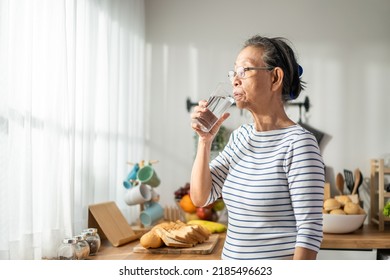 Asian Senior Mature Woman Drinking A Glass Of Milk In Kitchen At Home. Attractive Elderly Older Grandmother Holding And Sipping A Cup Of Milk After Waking Up In The Morning For Health Care In House.