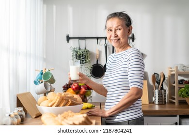 Asian Senior Mature Woman Drinking A Glass Of Milk In Kitchen At Home. Attractive Elderly Older Grandmother Holding And Sipping A Cup Of Milk After Waking Up In The Morning For Health Care In House.
