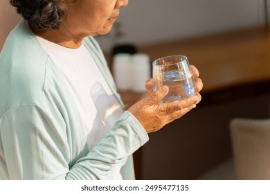 Asian senior mature woman drinking water from a glass after wake up on the bed in the morning. Elderly retired woman taking medicine or vitamins complex supplement at home. Healthcare concept. - Powered by Shutterstock