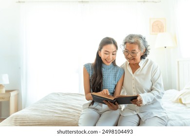 Asian senior mature woman reading a book with caregiver in bedroom. Happy elderly woman enjoy indoor activity lifestyle at home. Senior people mental health care, nursing and caregiving concept. - Powered by Shutterstock