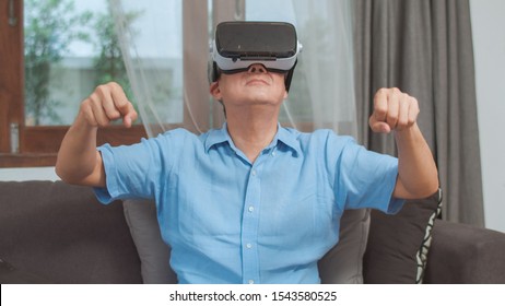 Asian Senior Men Play Games At Home. Asian Senior Older Chinese Male Happy Fun And Virtual Reality, VR Playing Games While Lying Sofa In Living Room At Home Concept.