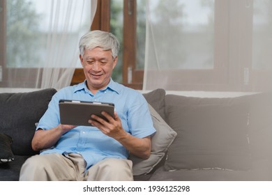 Asian senior men using tablet at home. Asian Senior Chinese male search information about how to good health on internet while lying on sofa in living room at home concept. - Powered by Shutterstock