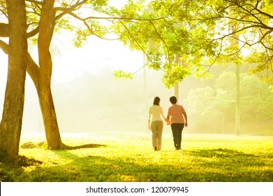 Asian Senior Mother And Adult Daughter Holding Hands Walking At Outdoor Park