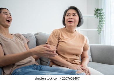 Asian Senior Mother Telling Joke To Her Daughter. Young Woman Laughing Of Funny Story On Couch At Home. Family Love Spending Time Together On Weekend