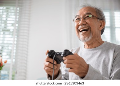 Asian senior old man enjoying holding joystick playing video game at home in living room, mature man hands using game controller, Funny on retirement elderly smile sitting on sofa life gaming - Powered by Shutterstock