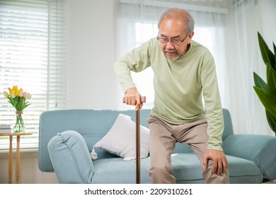 Asian Senior Old Man With Eyeglasses Type To Standing Up From Sofa With Walking Cane Stick To Walk At Home, Elderly Suffering From Knee Pain Ache Holding Handle Of Cane, Retirement Medical Healthcare