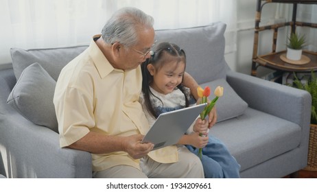 Asian senior old man looking to tablet computer and granddaughter come visitor at home, Grandfather reading news on digital tablet with his kid on sofa in living room - Shutterstock ID 1934209661
