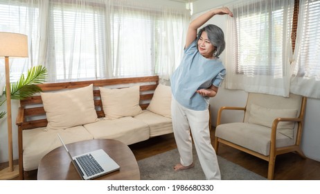 Asian Senior Older Woman Stay At Home, Working Out Follow Instructions Video From Online Trainer. Grandmother Doing Lockdown Activities In House Yoga, Pilates Exercise During Coronavirus Pandemic.