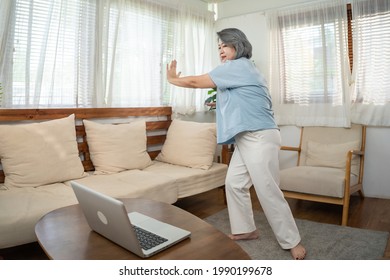 Asian Senior Older Woman Stay At Home, Working Out Follow Instructions Video From Online Trainer. Grandmother Doing Lockdown Activities In House Yoga, Pilates Exercise During Coronavirus Pandemic.