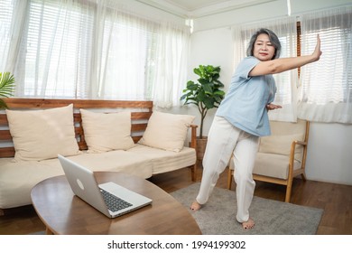 Asian Senior Older Woman Stay At Home, Working Out Follow Instructions Video From Online Trainer. Grandmother Doing Lockdown Activities In House Yoga, Pilates Exercise During Coronavirus Pandemic.