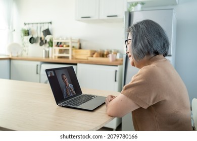 Asian Senior Older Woman Video Call With Doctor In Living Room At Home. Elder Patient Consulting With General Practitioner Application Computer Laptop. Doctor And Consultant Online And Telemedicine.