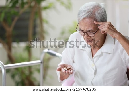 Asian senior patient with Alzheimer's disease or dementia,look at the pills capsules on her palm,trying to think,confused,old elderly people forget to take the medication,fail to remember or amnesia