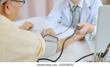 Asian Senior Patient Having Medical Exam With Doctor In Hospital. Doctor Adjusting Blood Pressure Gauge On Senior Gray-haired Man