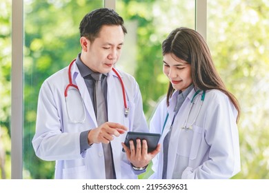 Asian Senior Professional Male Mentor Practitioner Doctor In White Lab Coat Uniform With Stethoscope Standing Helping Explaining Analyzing Data In Tablet Computer To Young Female Colleague