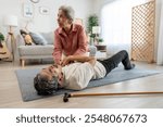 Asian senior wife helping elderly husband from falling on the ground. Attractive older man having an accident after feeling chest pain from heart attack then rescued by mature woman in living room.