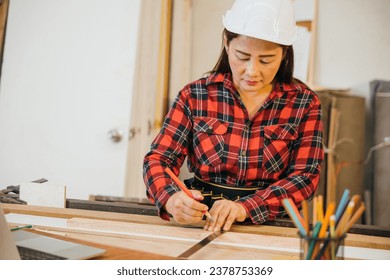 Asian senior woman carpenter taking measurement of a wooden plank and make in workshop, female holding ruler and use pencil drawing sign on plank at woodshop, National Carpenters Day - Powered by Shutterstock