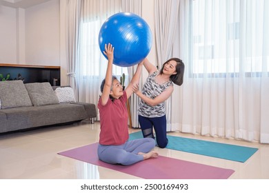 asian senior woman doing exercise with yoga ball,a young adult daughter help and support beside her,happy family doing yoga at home,domestic life,exercising  - Powered by Shutterstock