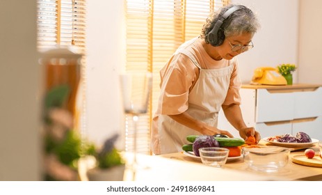 Asian senior woman enjoy healthy lifestyle learning to cook and making vegan food vegetable salad by watching online recipe on digital tablet with listening to the music with headphones in the kitchen - Powered by Shutterstock